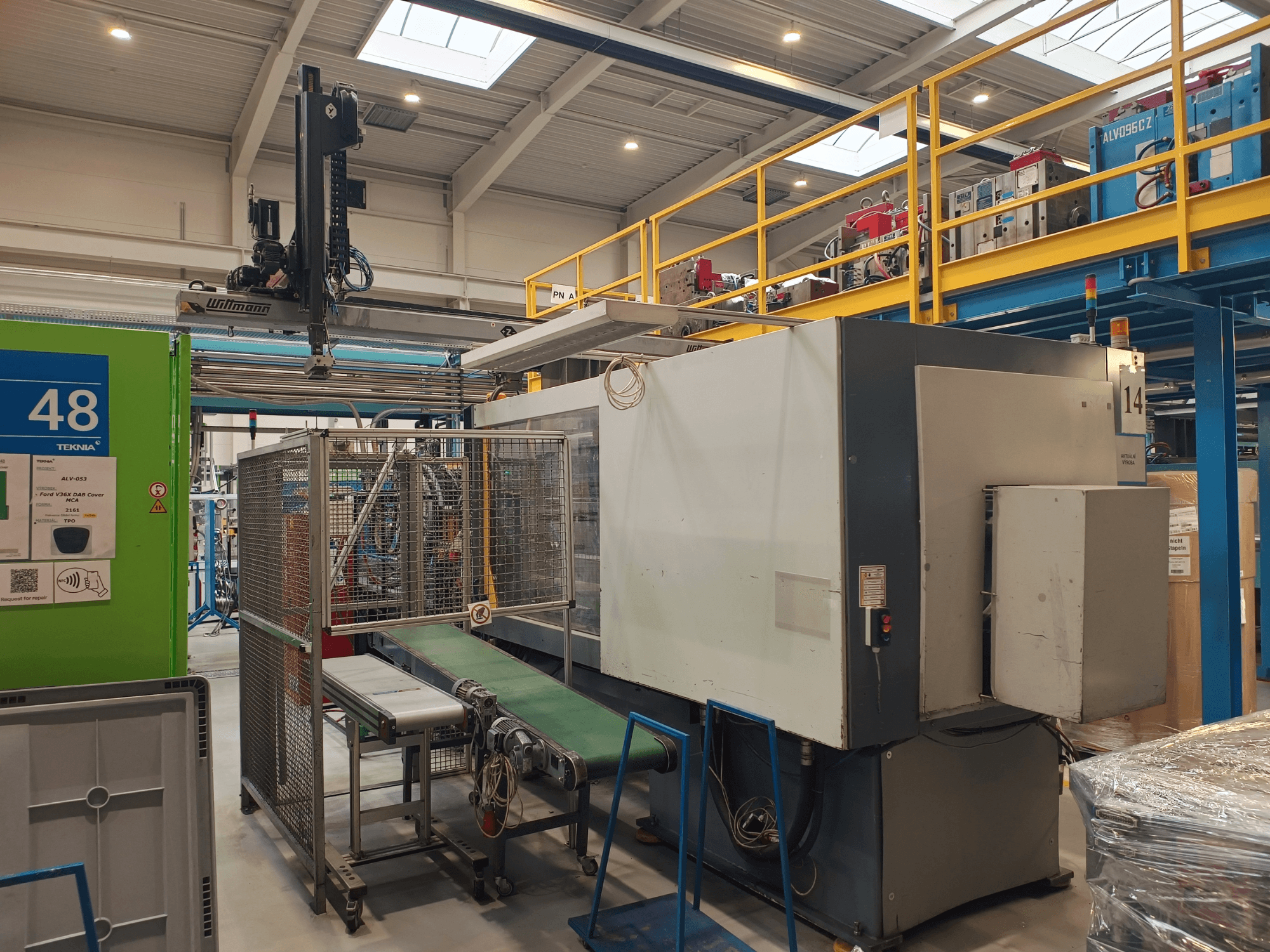 Industrial automation equipment with green conveyor, labeled '48', and overhead crane; side view of machine on factory floor.
